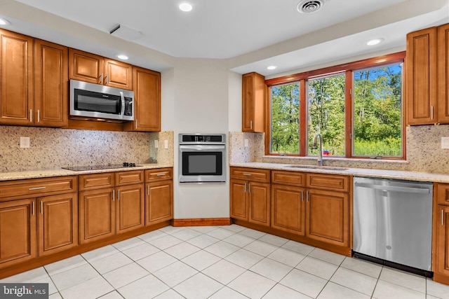 kitchen featuring appliances with stainless steel finishes, decorative backsplash, sink, and light stone countertops