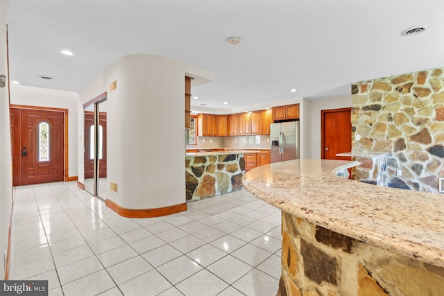 kitchen featuring stainless steel refrigerator with ice dispenser, light tile patterned floors, light stone counters, and tasteful backsplash