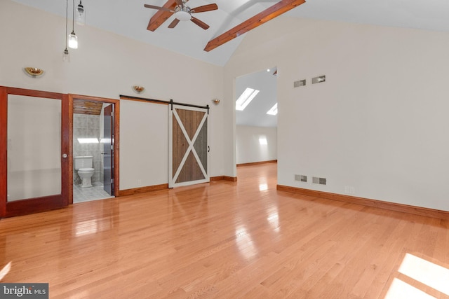 unfurnished room featuring ceiling fan, a skylight, light hardwood / wood-style flooring, high vaulted ceiling, and a barn door