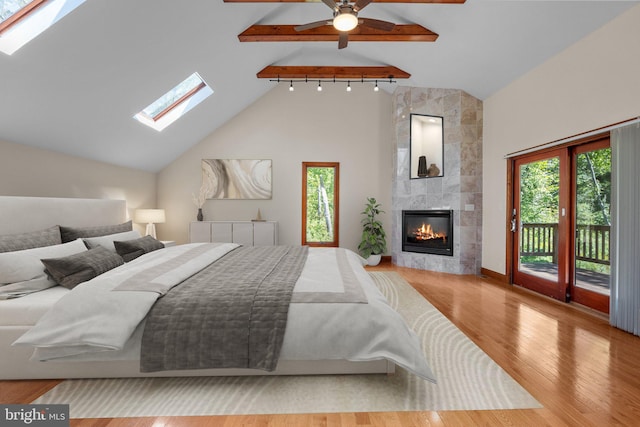 bedroom featuring hardwood / wood-style flooring, access to exterior, high vaulted ceiling, a large fireplace, and ceiling fan