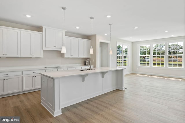 kitchen with black electric cooktop, hanging light fixtures, a center island with sink, and white cabinets