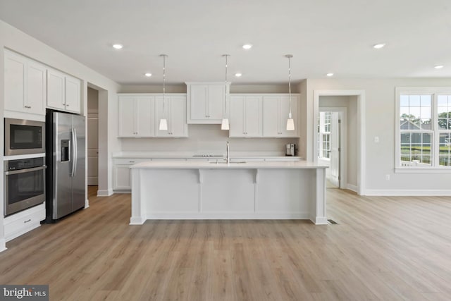 kitchen featuring an island with sink, appliances with stainless steel finishes, pendant lighting, and white cabinets