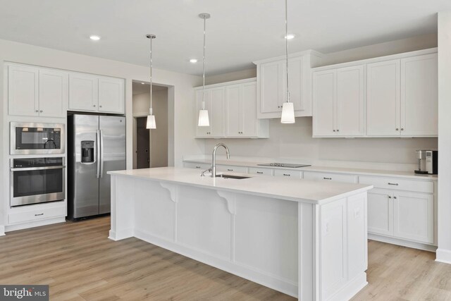 kitchen featuring an island with sink, hanging light fixtures, light wood-type flooring, and white cabinets