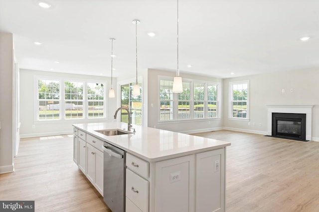 kitchen with sink, dishwasher, pendant lighting, light hardwood / wood-style flooring, and a center island with sink