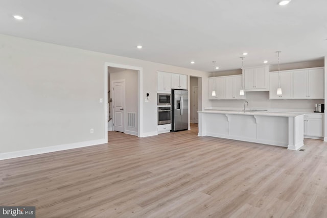 kitchen featuring light hardwood / wood-style flooring, white cabinetry, stainless steel appliances, an island with sink, and decorative light fixtures