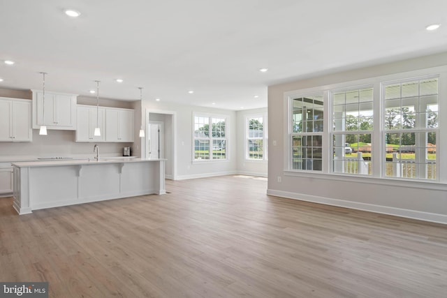 kitchen featuring white cabinetry, hanging light fixtures, light hardwood / wood-style flooring, and a center island with sink