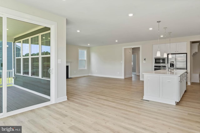 kitchen featuring white cabinetry, decorative light fixtures, light wood-type flooring, appliances with stainless steel finishes, and an island with sink