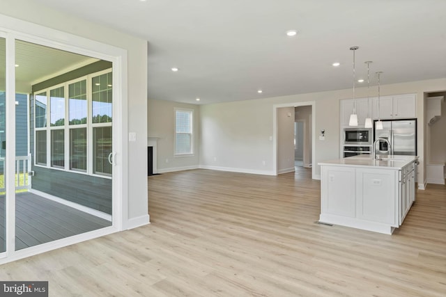 kitchen with hanging light fixtures, an island with sink, white cabinetry, light wood-type flooring, and stainless steel appliances