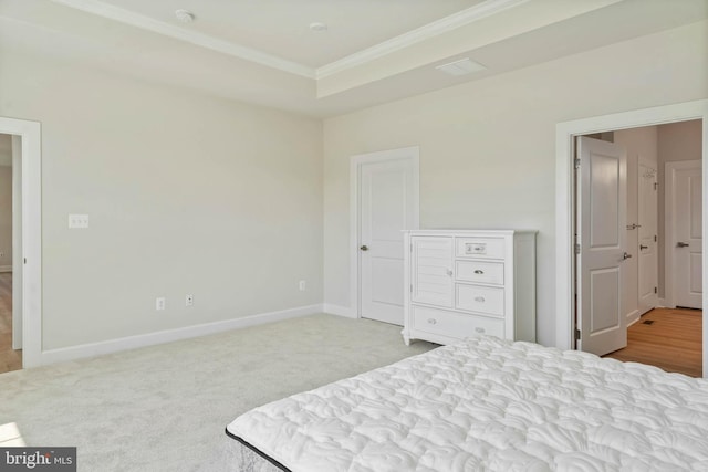 bedroom with ornamental molding, a tray ceiling, and light carpet