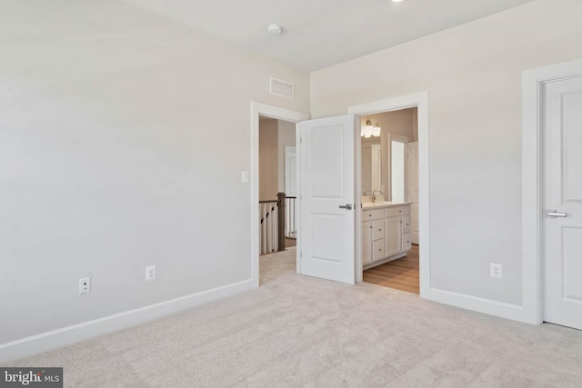 unfurnished bedroom with ensuite bathroom, sink, and light colored carpet