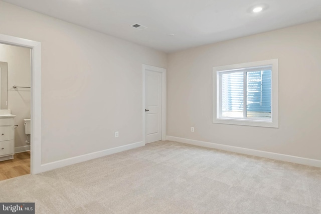 unfurnished bedroom with a walk in closet, light carpet, and ensuite bathroom