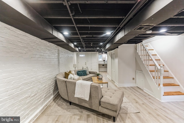 basement featuring light hardwood / wood-style flooring and brick wall