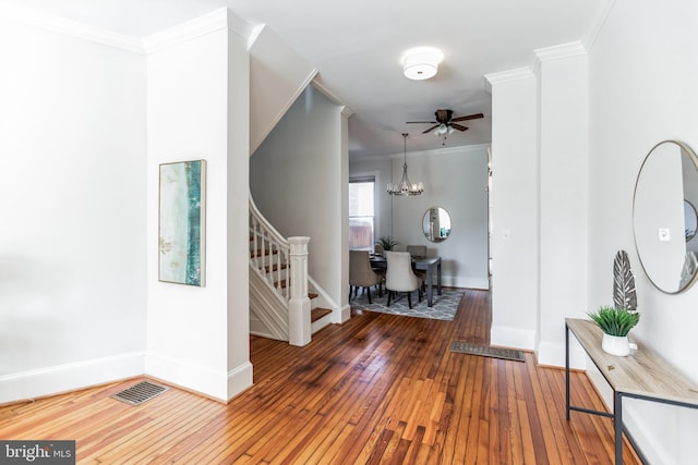 entryway featuring wood-type flooring, ceiling fan with notable chandelier, and ornamental molding