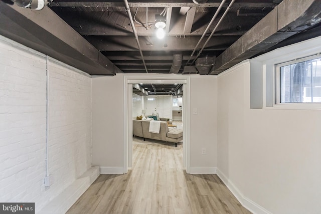 basement with light hardwood / wood-style flooring and brick wall