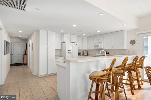 kitchen with light tile patterned flooring, white cabinetry, a kitchen breakfast bar, kitchen peninsula, and white appliances