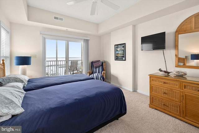 carpeted bedroom featuring access to outside, a tray ceiling, ceiling fan, and multiple windows