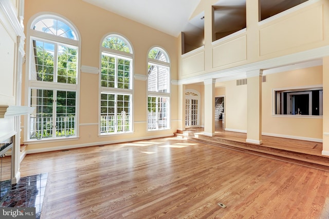 unfurnished living room featuring a premium fireplace, hardwood / wood-style flooring, ornate columns, and high vaulted ceiling