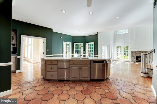 kitchen featuring a fireplace, dishwasher, sink, a center island with sink, and light hardwood / wood-style floors