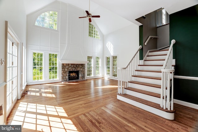 unfurnished living room featuring high vaulted ceiling, a healthy amount of sunlight, ceiling fan, and a stone fireplace