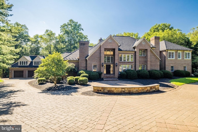 view of front facade featuring brick siding, a chimney, decorative driveway, and a garage