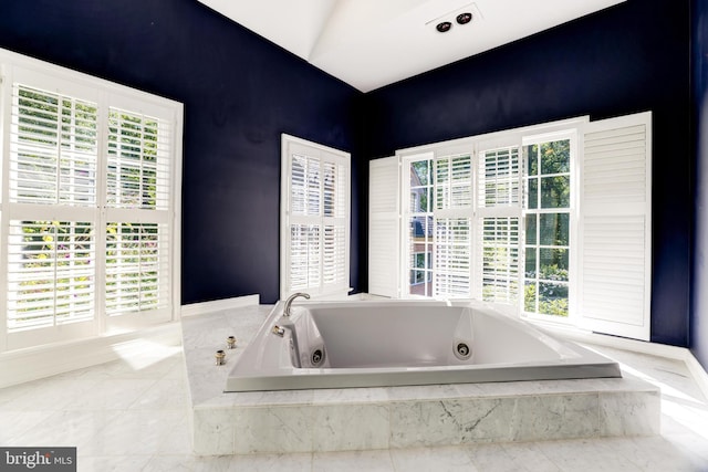 bathroom featuring vaulted ceiling, a wealth of natural light, and tiled bath