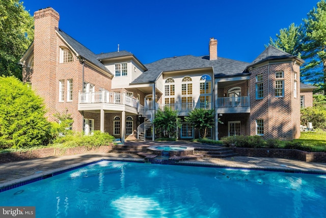 rear view of house with a balcony and a pool with hot tub