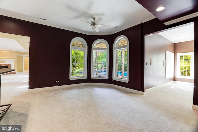 empty room with ornamental molding, a wealth of natural light, ceiling fan, and carpet floors