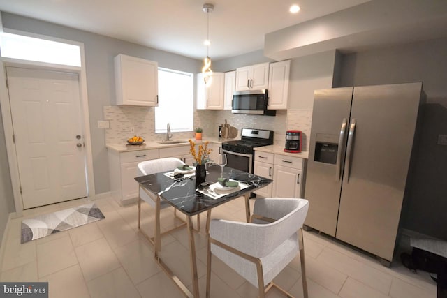 kitchen featuring pendant lighting, decorative backsplash, white cabinets, and appliances with stainless steel finishes