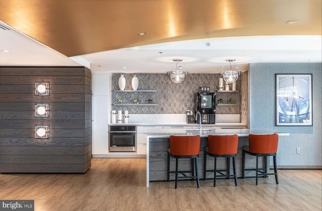 bar featuring stainless steel oven, white cabinetry, backsplash, pendant lighting, and hardwood / wood-style flooring