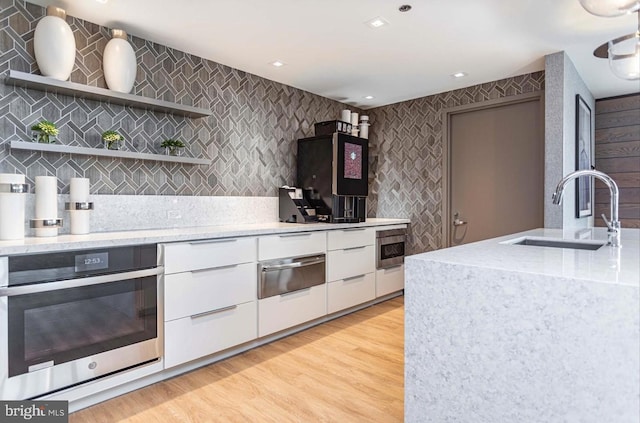 kitchen with white cabinets, appliances with stainless steel finishes, sink, and light hardwood / wood-style flooring