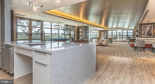 kitchen featuring light hardwood / wood-style floors, sink, a kitchen island with sink, light stone countertops, and white cabinetry