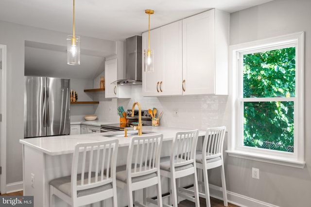 kitchen featuring stainless steel appliances, kitchen peninsula, decorative light fixtures, and wall chimney exhaust hood