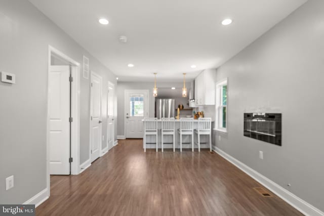 interior space featuring white cabinets, decorative light fixtures, stainless steel fridge, dark wood-type flooring, and a breakfast bar area