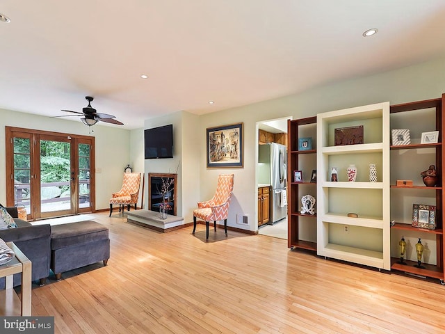 living room featuring ceiling fan, light wood-type flooring, and built in shelves