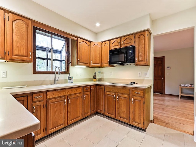 kitchen with light tile patterned floors, a sink, light countertops, brown cabinets, and black appliances