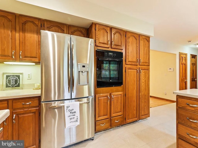 kitchen with brown cabinets, stainless steel refrigerator with ice dispenser, light countertops, oven, and baseboards