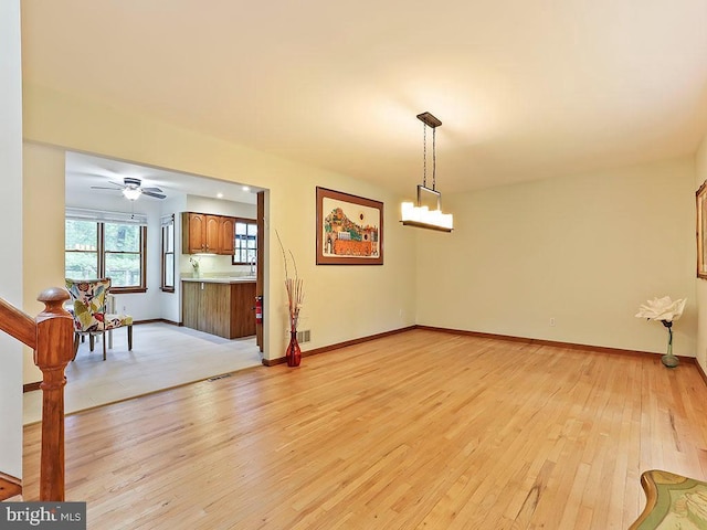 interior space with light wood-style floors, baseboards, and ceiling fan with notable chandelier