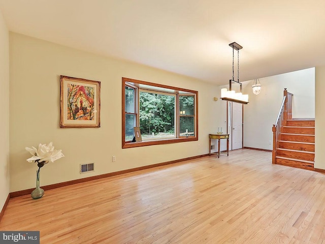 unfurnished room with light wood-style floors, baseboards, stairs, and visible vents