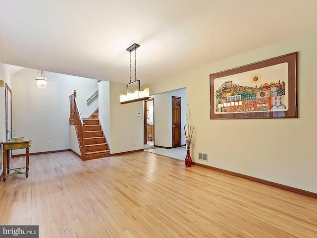 interior space featuring a notable chandelier, visible vents, light wood-type flooring, baseboards, and stairs