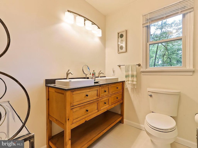 bathroom with double vanity, a sink, toilet, and baseboards