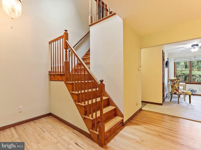 stairs featuring a ceiling fan, a high ceiling, baseboards, and wood finished floors