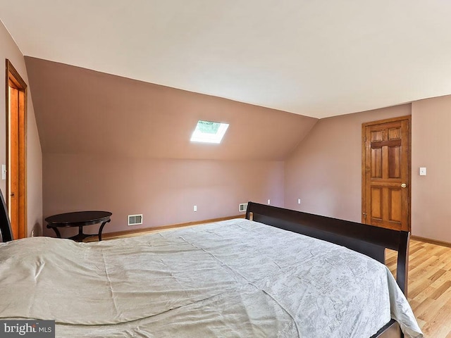 bedroom featuring vaulted ceiling with skylight, visible vents, baseboards, and wood finished floors