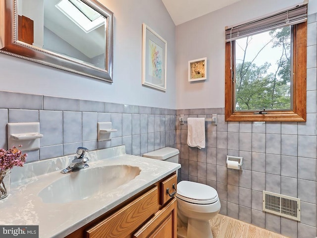 bathroom with visible vents, toilet, lofted ceiling with skylight, vanity, and tile walls