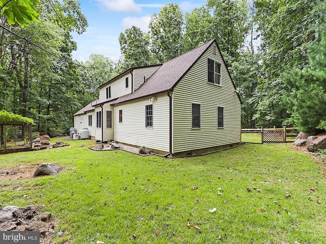 rear view of property featuring a shingled roof, fence, and a lawn