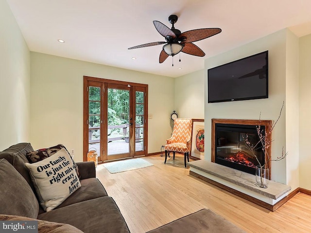 living area featuring a glass covered fireplace, baseboards, and wood finished floors