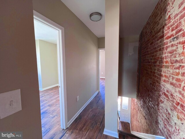 corridor featuring dark wood-type flooring and brick wall