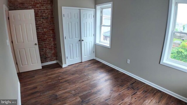 unfurnished bedroom featuring dark hardwood / wood-style flooring, multiple windows, and a closet