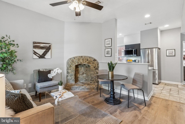 living room with ceiling fan, a stone fireplace, and light wood-type flooring