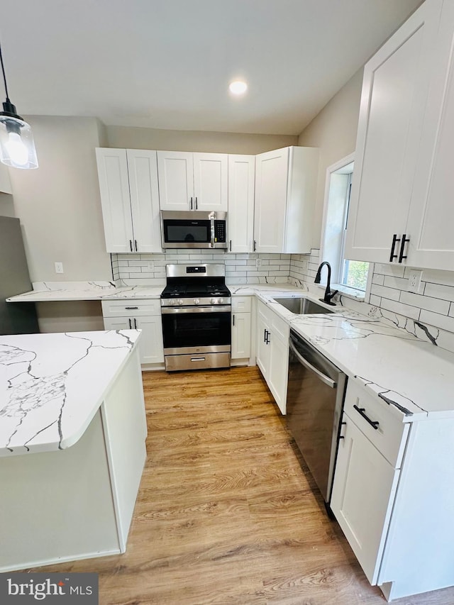 kitchen featuring appliances with stainless steel finishes, a sink, white cabinetry, and light stone countertops