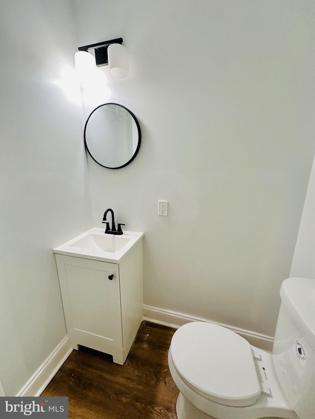 half bath with toilet, baseboards, wood finished floors, and vanity